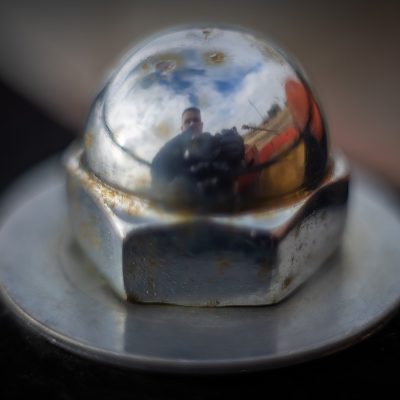 Close-up of a reflective chrome dome nut showing a photographer's reflection.