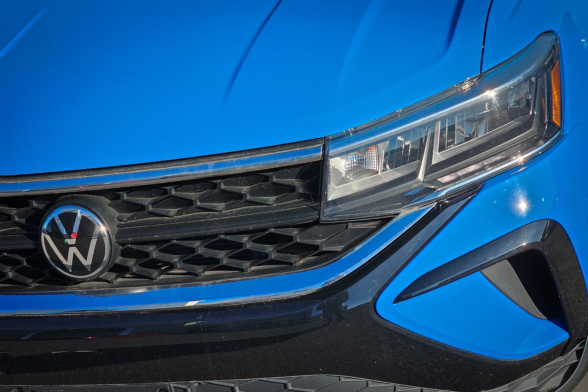 A close-up shot of a bright blue Volkswagen's front end, featuring the honeycomb grille with the VW logo and a modern headlight housing.